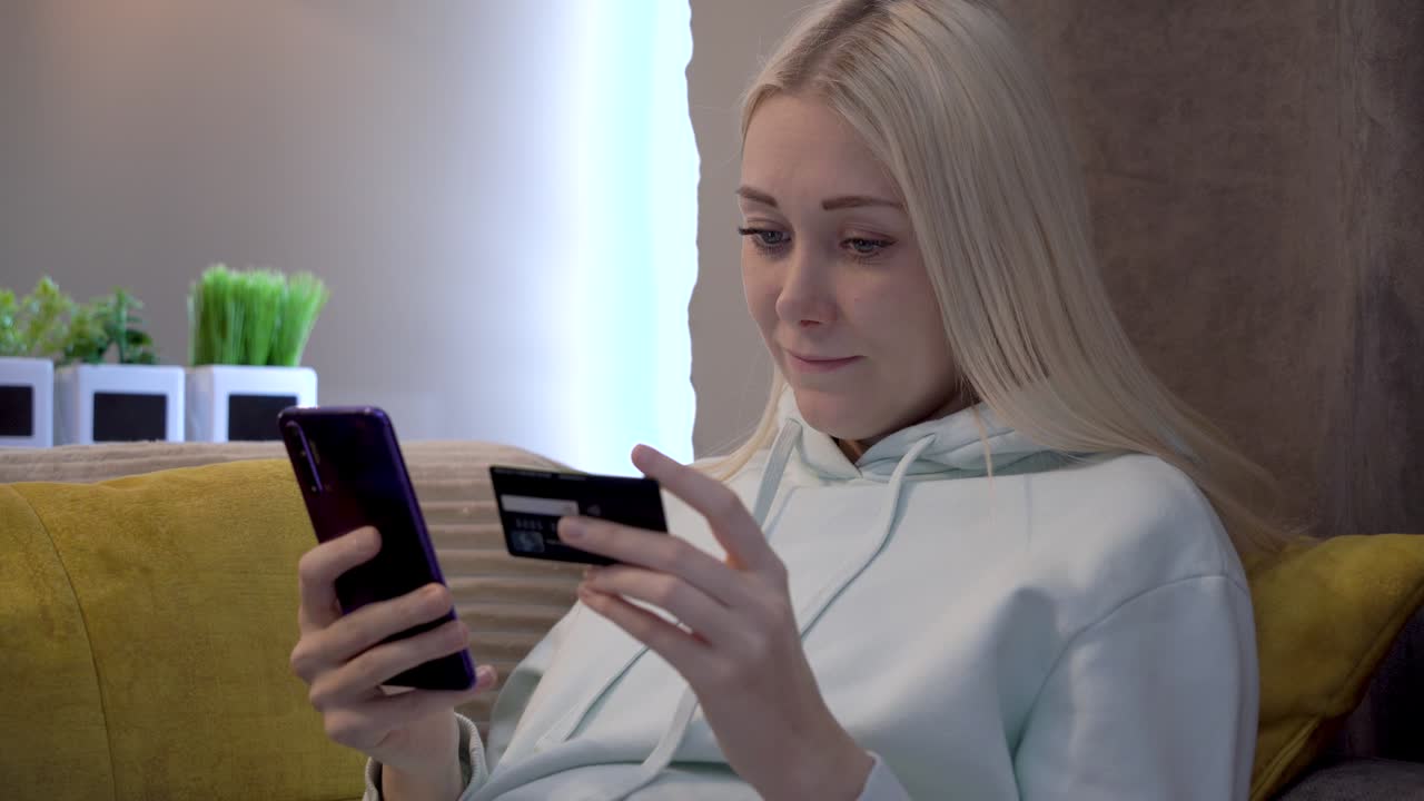 joven cliente femenina usando el teléfono móvil mientras está sentada en el sofá en casa.