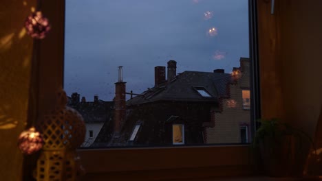 dusk view from window overlooking european rooftops, warm indoor lighting contrasts with the cool blue of twilight, reflective mood, timelapse