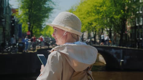 dynamic life of the city. a woman with headphones and a smartphone in her hand, in the background an intense movement of cyclists, pedestrians and ships on the canal of amsterdam