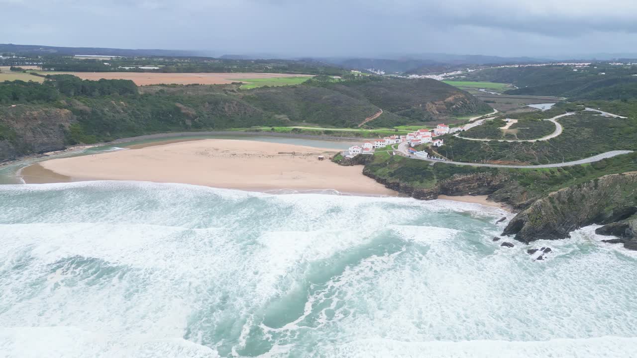 Sweeping beach with waves, cliffside village and lush hills in Aljezur, Portugal