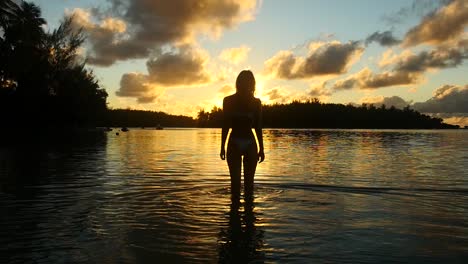 Niña-Parada-En-El-Agua-Durante-La-Puesta-De-Sol-En-La-Polinesia-Francesa.-Silueta-De-Mujer