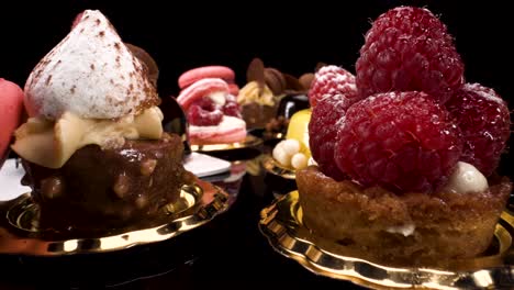 macro view moving past patisserie on black reflective background, probe lens view of sweet pastry and small cakes