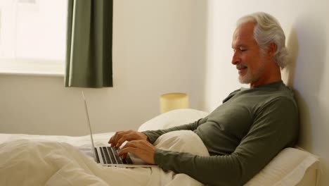 senior man using laptop on bed in bedroom 4k