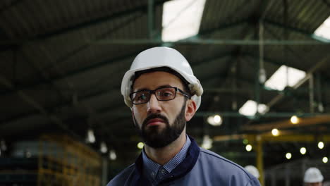 close-up view of the male factory worker wearing a helmet and glasses walking in a big factory