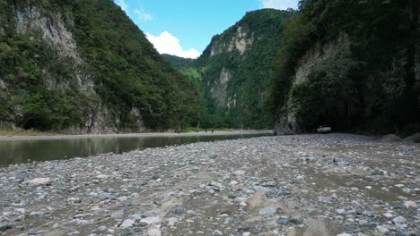 Low-flight-over-riverbank-at-Muchas-Aguas-with-people-relaxing-in-background,-Dominican-Republic