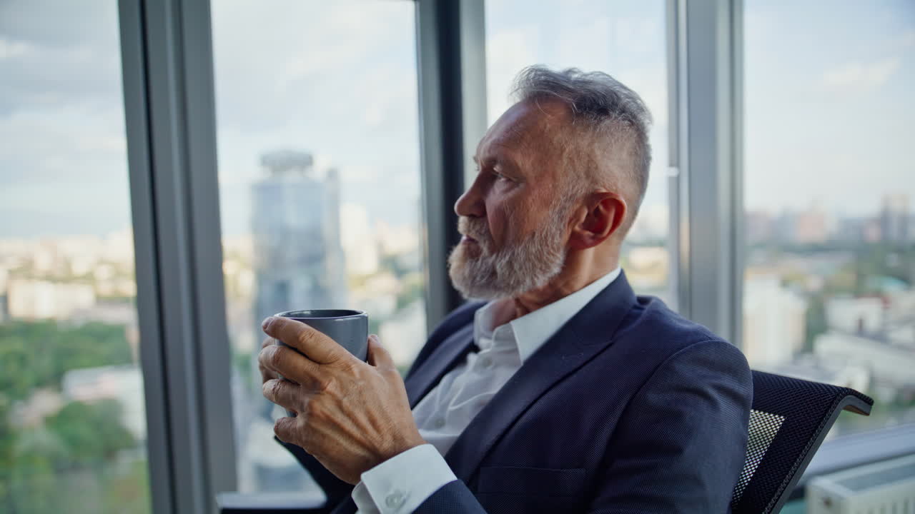 Primo piano di un uomo d'affari maturo che beve caffè guardando la vista sulla città dalla finestra dell'ufficio