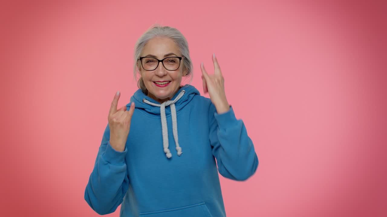 Overjoyed delighted crazy elderly woman showing rock n roll gesture by hands, cool sign, dancing
