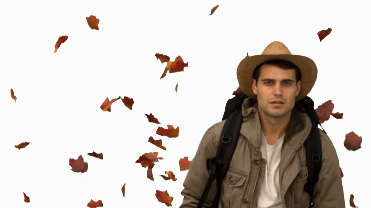 Uomo con un cappello che cammina sotto foglie che cadono su schermo bianco