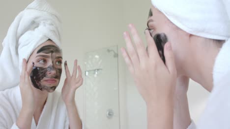 caucasian woman with towel on head making face mask in bathroom in slow motion