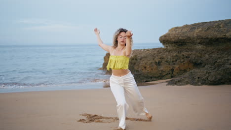 curly girl dancing seashore in front ocean waves. female dancer moving body