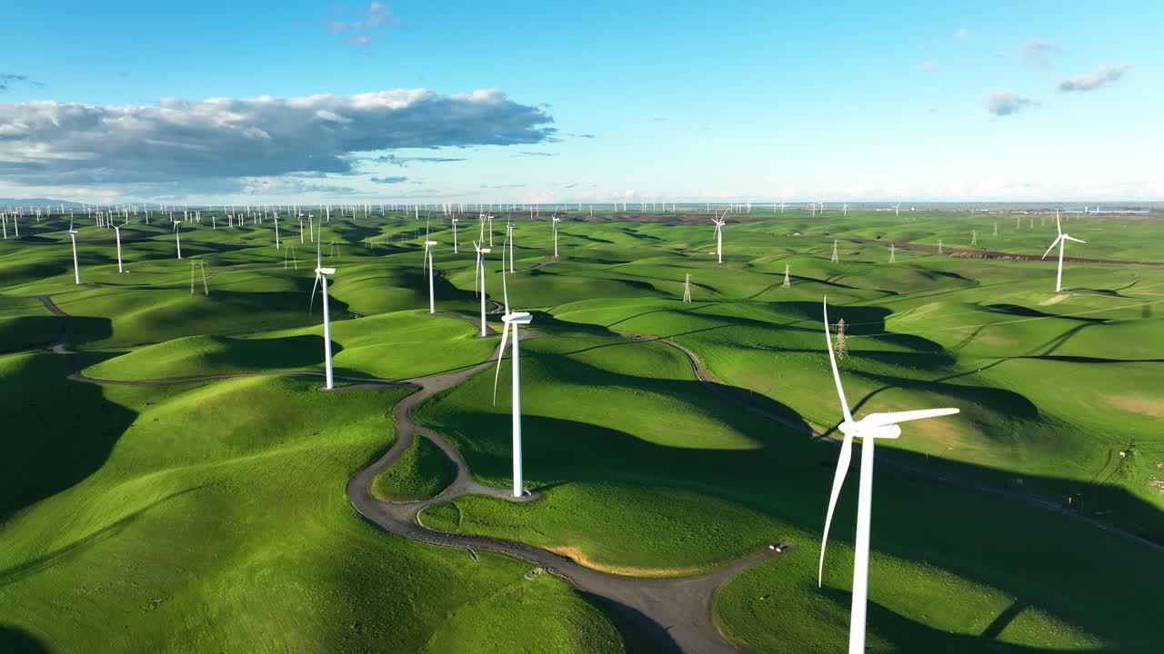 Aerial view of Wind Turbine Farm in slow motion on green rolling hills ...