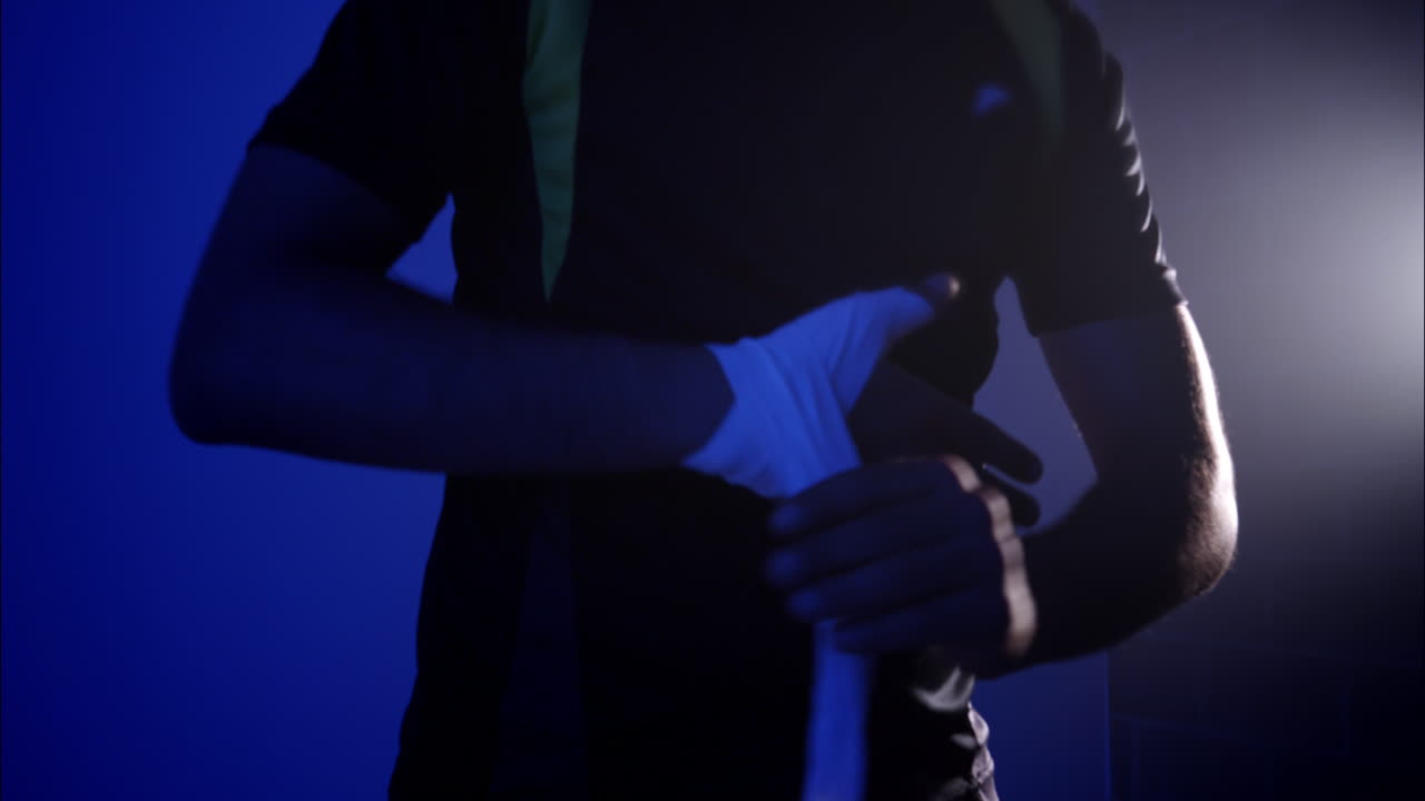 Man Wrapping Hands with Boxing Wraps in Dark Blue Gym