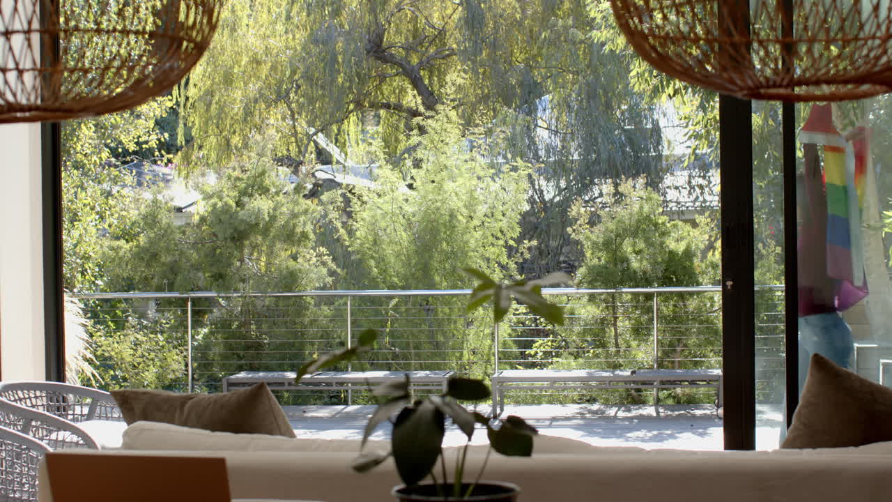 Looking through window, woman enjoying view of lush green garden from living room