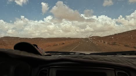 Wipers-dry-windscreen-from-raindrops-as-car-drives-on-desert-road-in-Tunisia,-driver-point-of-view