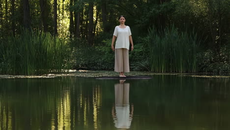 woman practicing yoga and meditation poses on a platform in a serene lakeside forest