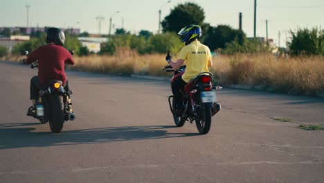 An-instructor-in-a-yellow-T-shirt-and-helmet-rides-Near-his-student-in-a-red-T-shirt-and-helmet-on-a-motorcycle.-School-day-at-the-driving-school