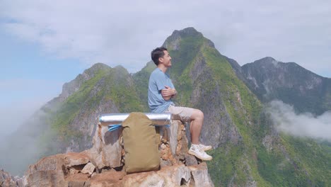 asian hiker male with a backpack sitting on the rock enjoys seeing beautiful view of top foggy mountain