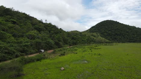 Vista-Aérea-De-Un-Camión-Que-Se-Mueve-Por-Un-Camino-De-Tierra-En-El-Paisaje-De-Guyana,-Entre-La-Selva-Tropical-Y-El-Prado-Verde,-Disparo-De-Drones
