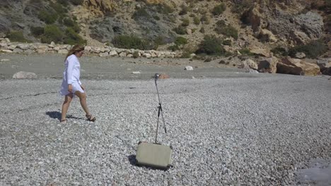 Toma-Aérea-Sobre-Una-Mujer-Cantando-En-La-Playa-Con-Un-Vestido-Blanco-Y-Un-Micrófono-Vintage