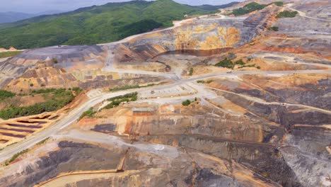 aerial approaching shot of gold silver mine during sunny day in dominican republic. wide shot. street and roads with green mountains in distance.