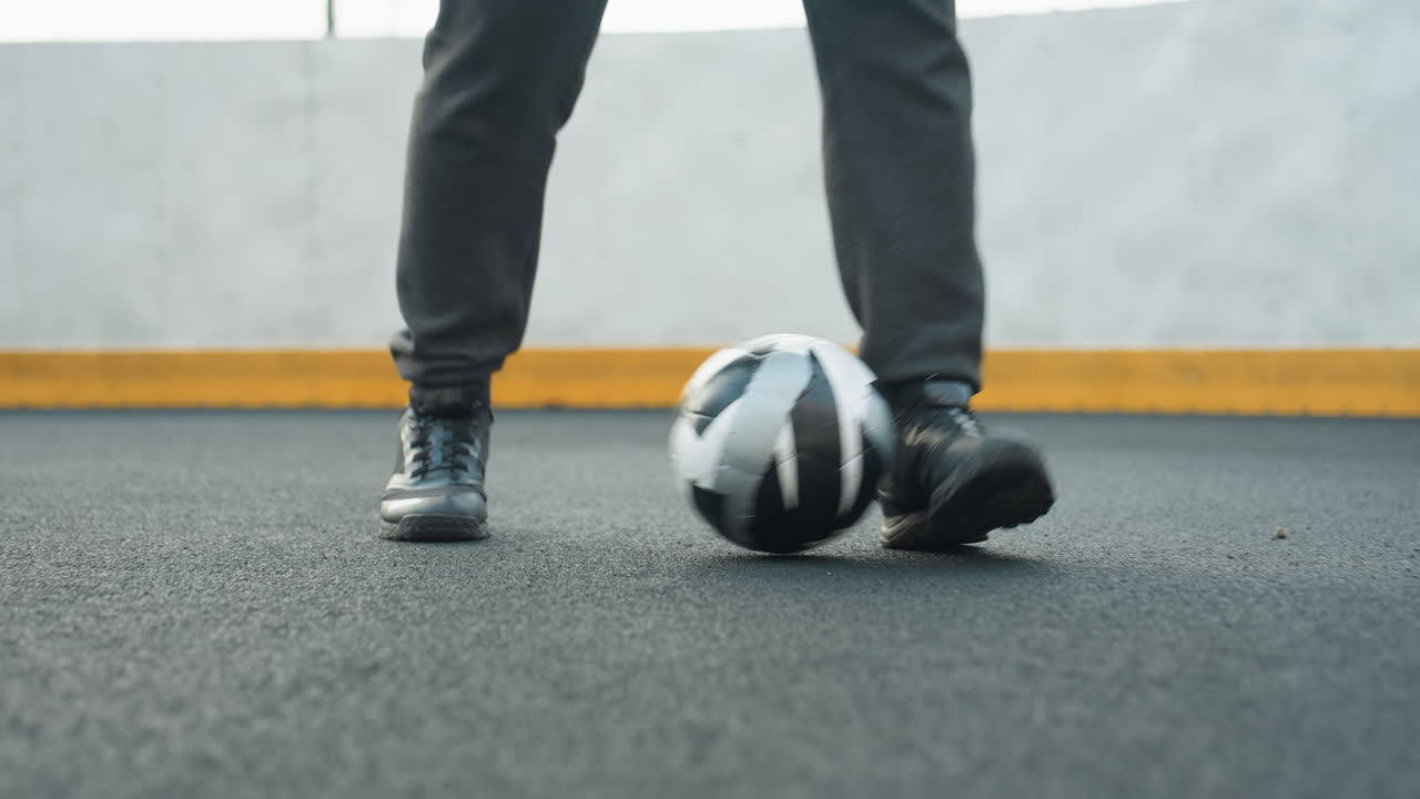 Close-up of man skillfully controlling soccer ball with feet on sport arena, showcasing precise footwork and athletic shoes, background features yellow barrier