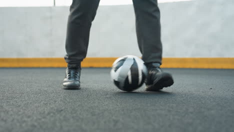 close-up of man skillfully controlling soccer ball with feet on sport arena, showcasing precise footwork and athletic shoes, background features yellow barrier