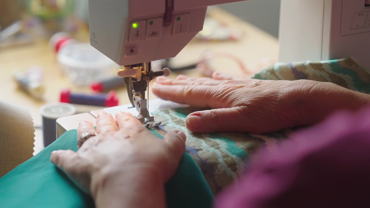 Woman sews two blue pieces of fabric together on sewing machine, close up, indoor setting