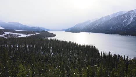 Lago-Nevado-Muncho-En-Invierno-Con-Bosque-Verde,-Seguimiento-De-Disparos-De-Drones