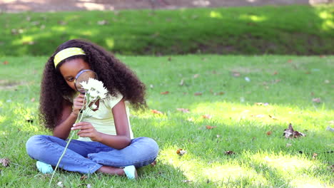 Little-girl-sitting-on-grass-inspecting-a-flower