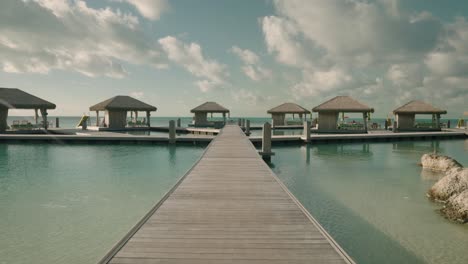 pristine cabanas over water on tropical island push in on dock on sunny summer day, perfect resort vacation in 4k