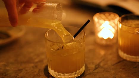 a cocktail is poured into a glass in a dimly lit bar setting, creating a warm, inviting atmosphere