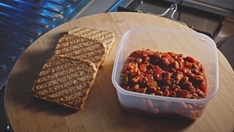 Pollo-Picante-Con-Frijoles-En-Un-Recipiente-De-Comida-Con-Rebanadas-De-Tostadas-Integrales-Al-Lado