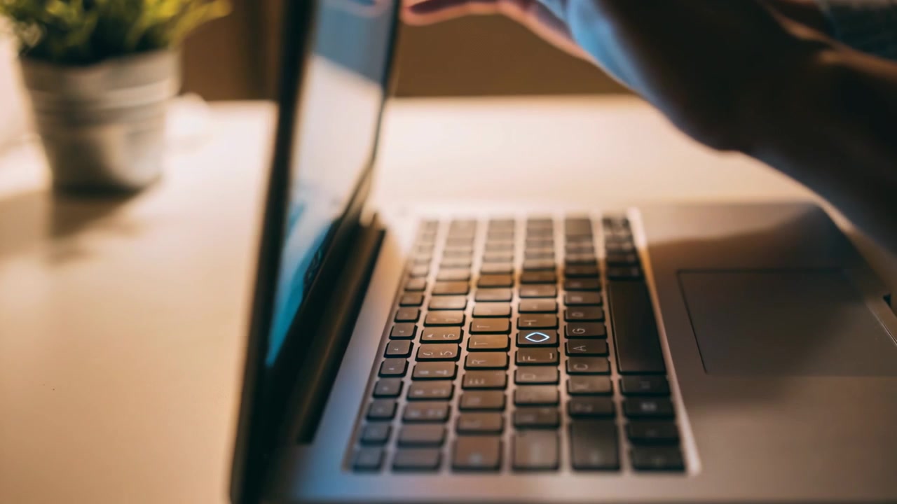 Typing adult hands pausing then closing laptop lid on home office desk, plant left ending work