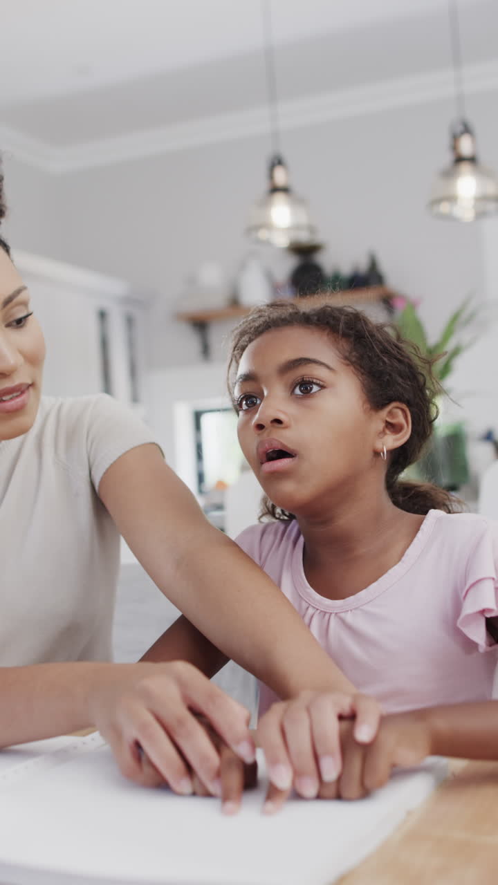 Vertical video of biracial mother and daughter reading braille, slow motion