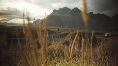 Wanderer-stands-in-the-distance-on-a-black-sanded-dune-in-a-grassy-mountain-landscape