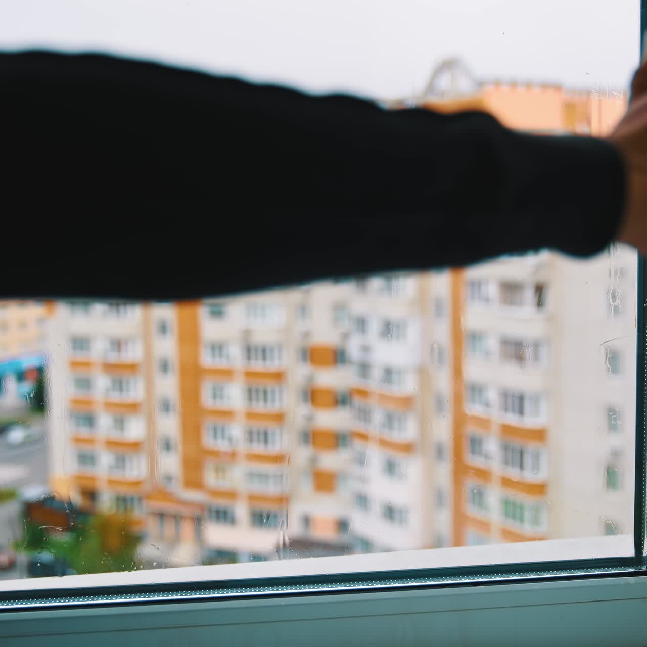 Window cleaning in flat. Housewife washes window with a cleaning brush on urban buildings background. Householding