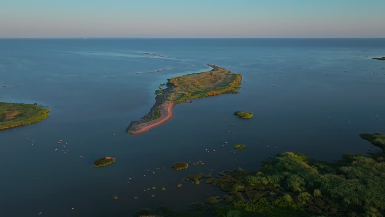 Drone shot of green island islet in summer, moving right to left revealing green coastline on a peaceful coast