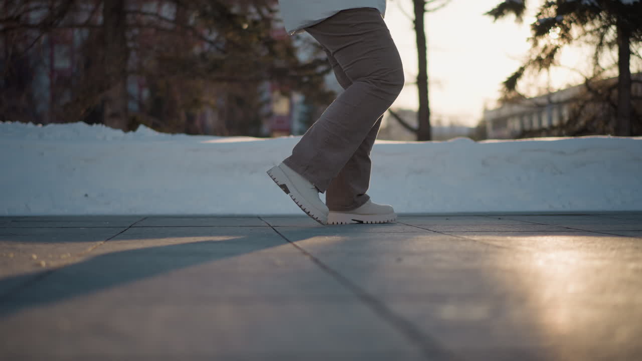 Leg view of dancer moving legs on tiled pavement near snow under golden sunset light capturing rhythmic winter motion with shadow play and textured ground for dynamic outdoor performance