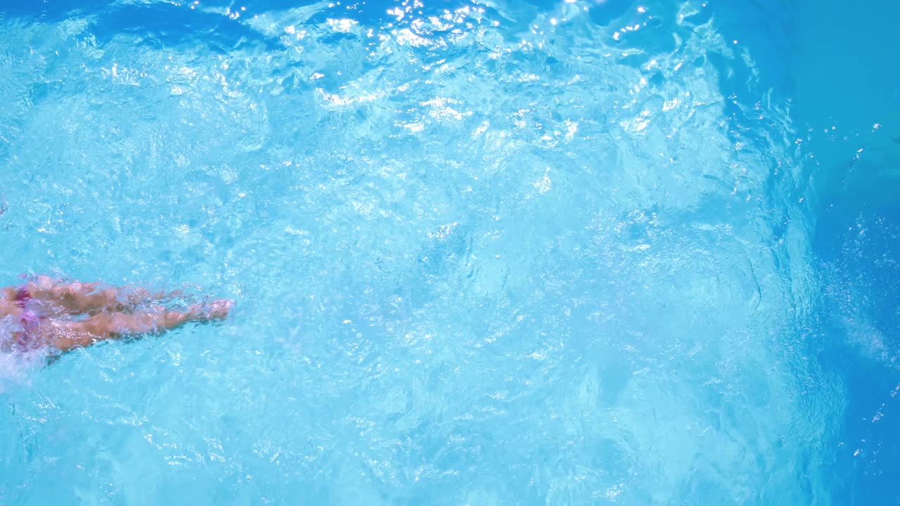 Pemandangan dari atas: wanita berambut cokelat berenang di kolam pada hari yang cerah