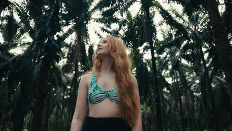 Woman in a bikini top standing among palm trees