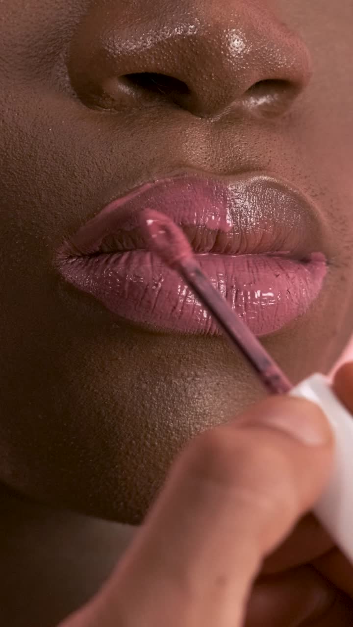 Visagiste applying lip gloss while doing makeup on black transgender model. Vertical footage