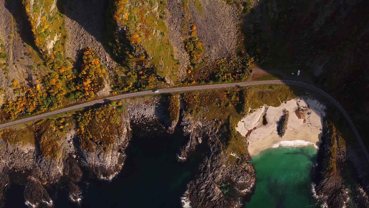 Winding road along a cliffside with rocky coastline, clear turquoise water below