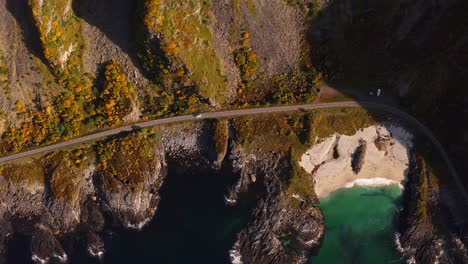 winding road along a cliffside with rocky coastline, clear turquoise water below