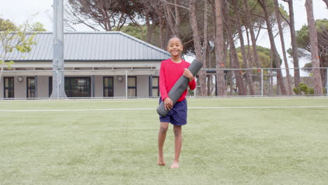 boy holding yoga mat on school field, looking content