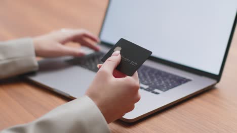 close up woman holding bank card shopping online on laptop with mock-up blank screen, using web banking system