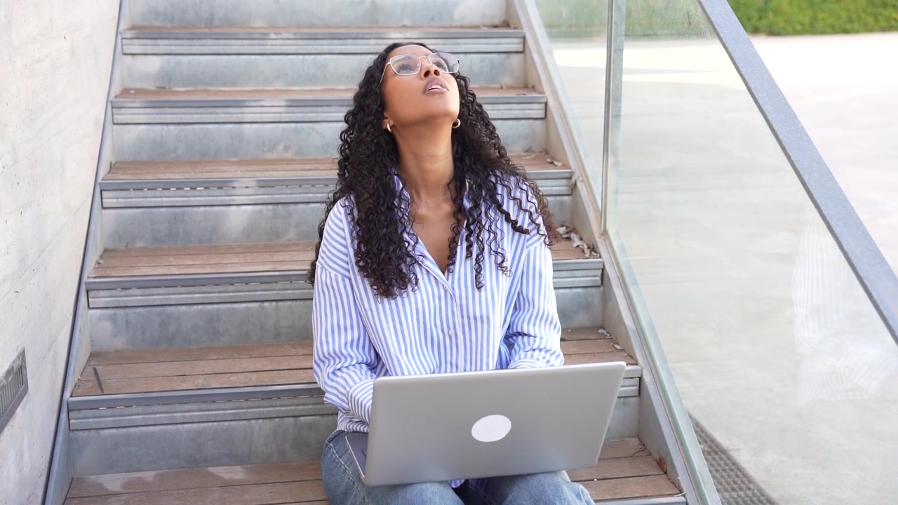 Una donna stressata intenta a lavorare al suo laptop mentre è seduta sulle scale in un ambiente urbano.