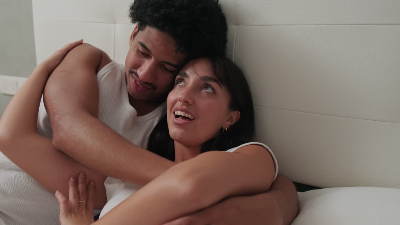 Pareja joven feliz acurrucándose y abrazándose en la cama