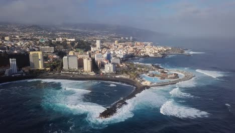 aerial panorama of puerto de la cruz resorts and pools surrounded by sea waves, tenerife, canary islands, spain.