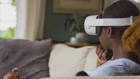 Woman-Relaxing-Lying-On-Sofa-At-Home-Wearing-VR-Headset-And-Interacting-With-AR-Technology