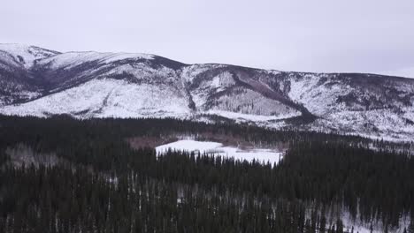 Wide-Aerial-Orbit-of-Frozen-Pond-in-Alaska,-Wintertime,-Snow-Capped-hills-in-the-background